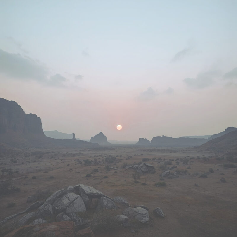 A hazy morning over a vast, empty dry landscape, with a pale sun low above the distant horizon.